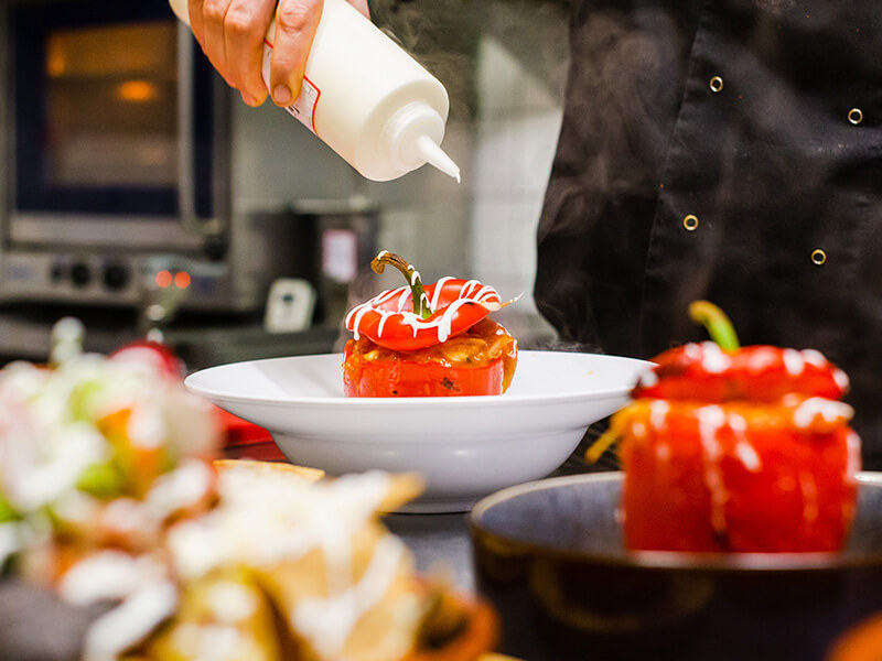 Chef adding cream to stuffed red pepper dish